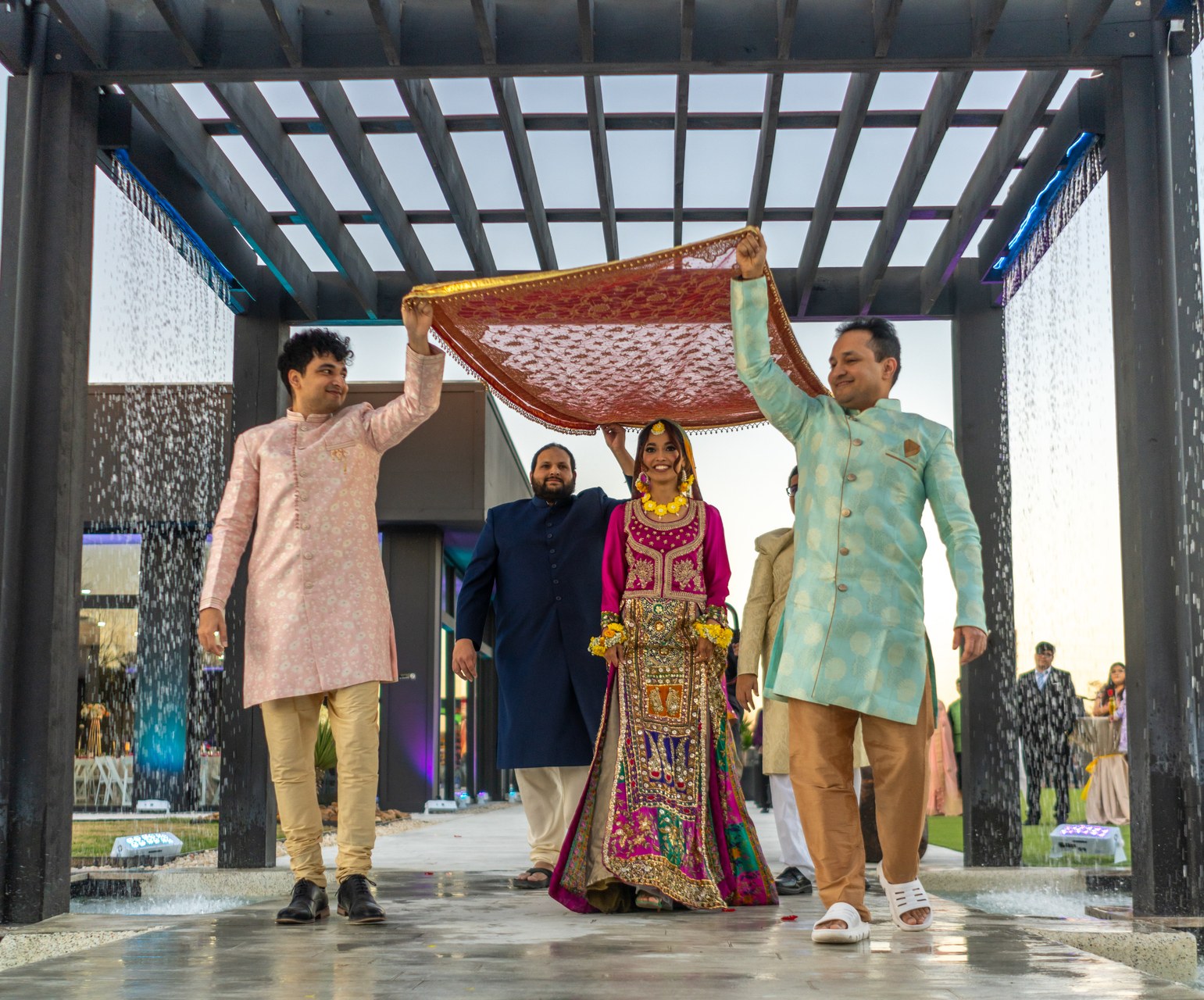 Indian bride procession under water pergola at dusk